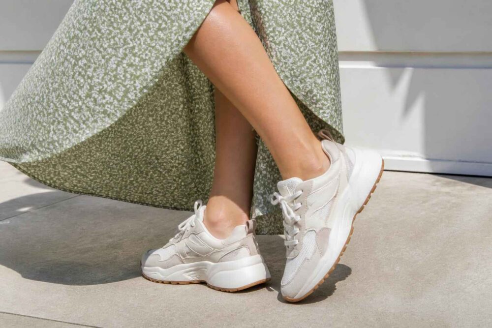 Kobieta w białych sneakersach i zielonej sukience stojąca na słońcu