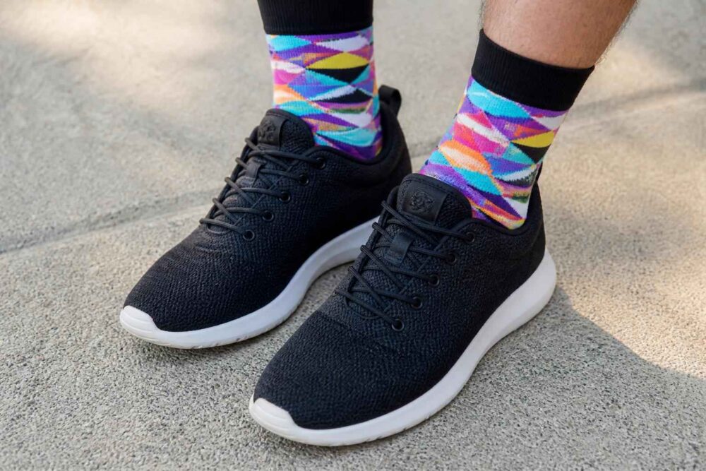 Czarne sportowe buty na stopach w połączeniu z kolorowymi skarpetkami we wzory geometryczne