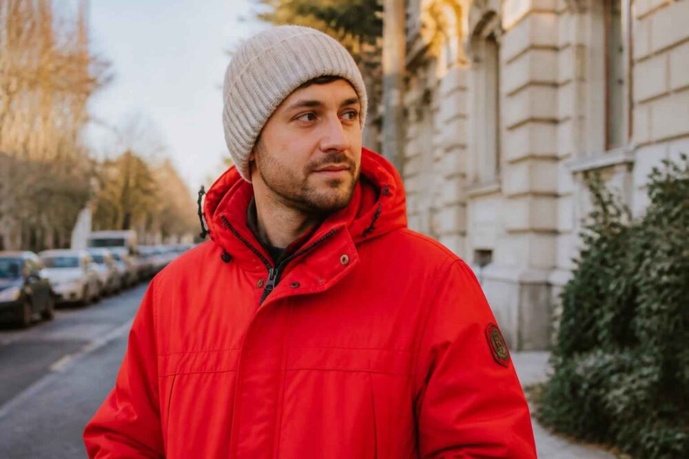 Mężczyzna w czerwonej kurtce i szarej wełnianej czapce na miejskiej ulicy